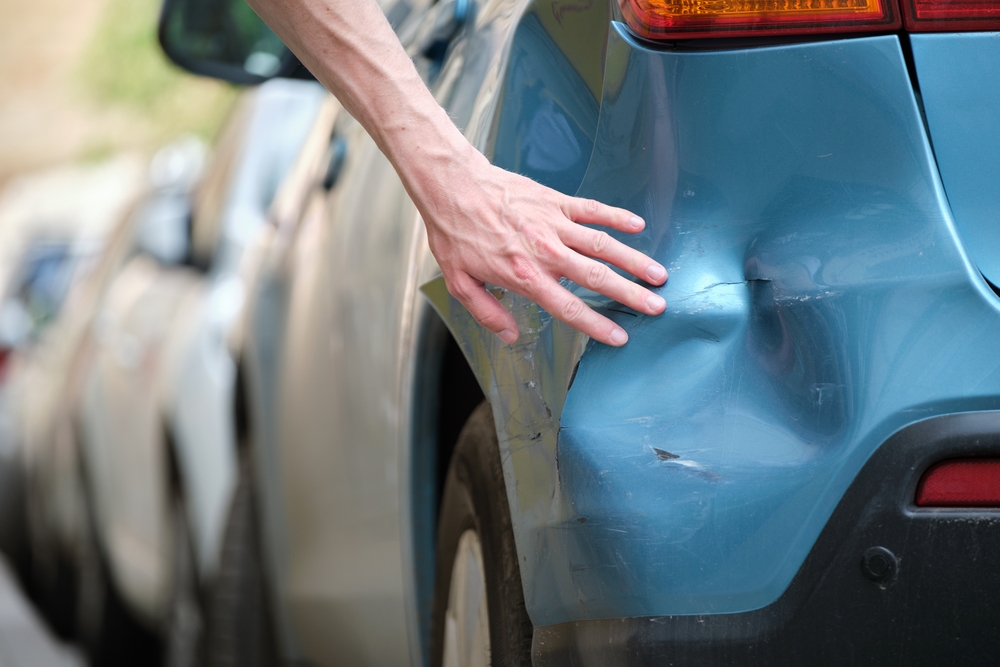 Driver,hand,examining,dented,car,with,damaged,fender,parked,on